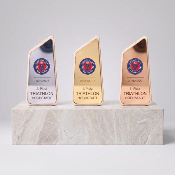 Personalisierter Holz-Pokal Eine moderne, asymmetrisch gestaltete Trophäe mit einem hellen Holzrahmen, der eine glänzende, metallische Platte einfasst. Im oberen Drittel befindet sich ein rundes Emblem mit einem roten Emaille-Hintergrund, das zwei Tennisspieler beim Spiel zeigt. Darunter folgen eingravierte horizontale Linien und der Text: "2026", "1. Platz", "Tennisturnier", "Altersklasse ab 30". Die Trophäe steht auf einer weißen Oberfläche.